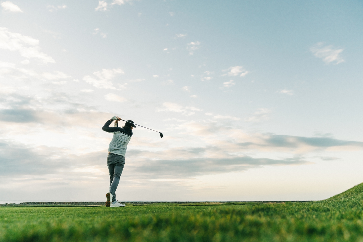 Male golfer swinging club at course during sunset