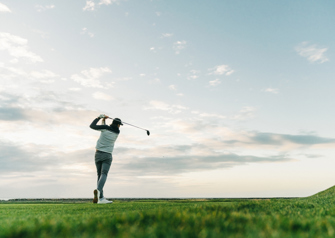 Male golfer swinging club at course during sunset