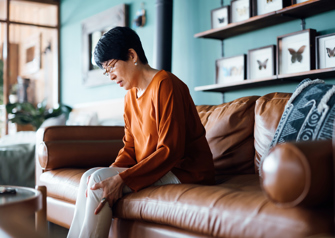 A distraught senior Asian woman feeling unwell, suffering from pain in leg while sitting on sofa in the living room at home