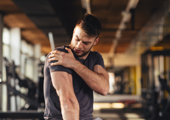 man in the gym looking at his injured shoulder