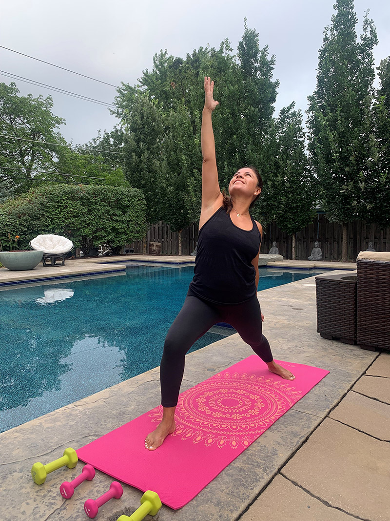 Woman doing yoga on yoga mat next to in ground pool